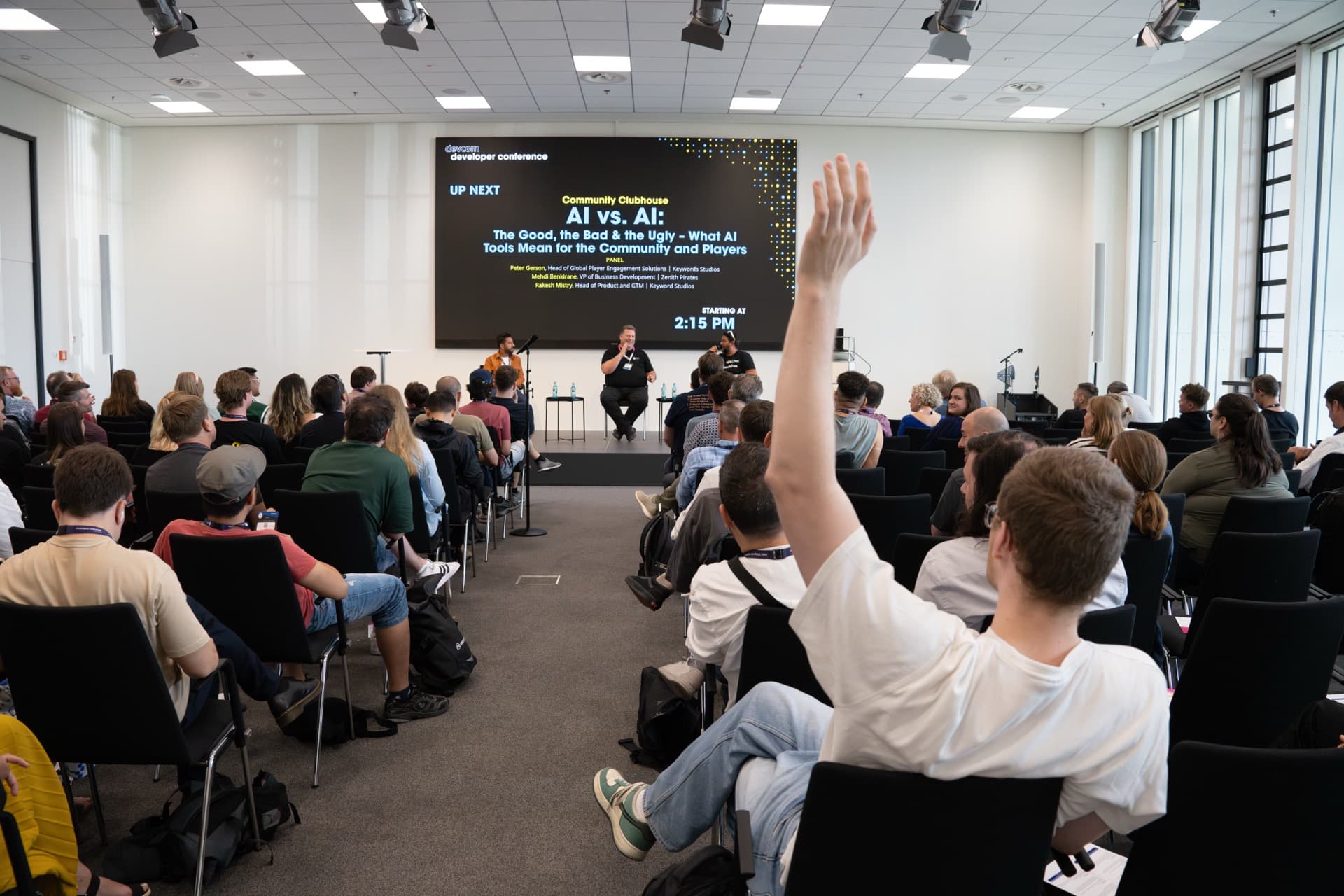 A packed Community Clubhouse session at devcom 2025 in Cologne, AI vs. AI panel with audience hands raised